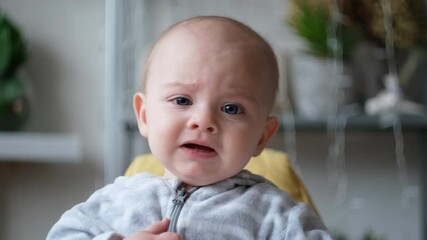 Upset little baby crying indoors. Infant baby boy closeup. Tired kid weeping and crying.