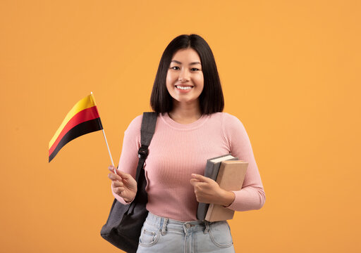 Teen happy asian woman with backpack holds notebooks and small flag of Germany