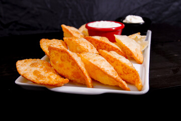 Deliciosos pasteis de carne, camarão, queijo com creme de queijo gorgonzola em recipiente branco em fundo escuro.