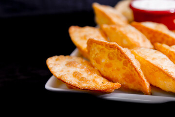 Deliciosos pasteis de carne, camarão, queijo com creme de queijo gorgonzola em recipiente branco em fundo escuro.