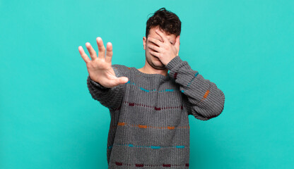 young man covering face with hand and putting other hand up front to stop camera, refusing photos...