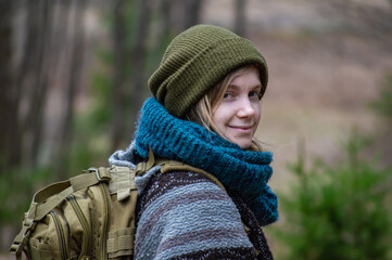Portrait of a young woman with layers of heavy winter clothes, wool scarf and hat turning to look at camera and smiling during a country hike.