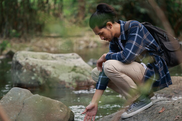Close up young adult human Asian man touching stream water in the forest while he hiking, peaceful serenity moment with nature.