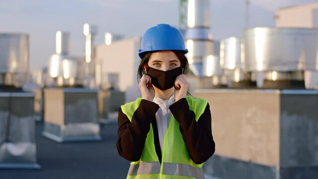 Charismatic lady architect on the construction site in front of the camera take the protective mask and wearing on face in pandemic of Coronavirus in front of the camera