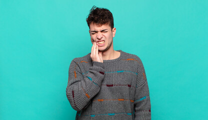 young man holding cheek and suffering painful toothache, feeling ill, miserable and unhappy,...