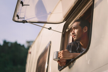 Fototapeta na wymiar Handsome young Asian man, traveler on road trip, sit inside camping van in the morning. Cosy comfortable setup in camper trailer or van. Millennial travel trend, adventure on the road