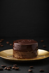 Austrian cake, sackertorte. Chocolate cake on a golden plate. Coffee beans on a black textured table. Side view of a chocolate dessert.