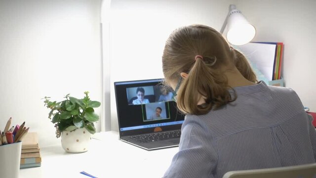 Cute school girl at online lesson with her teacher using laptop during digital homeschooling