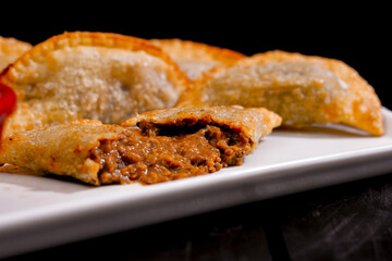 Deliciosos pasteis de carne, camarão, queijo com creme de queijo gorgonzola em recipiente branco em fundo escuro.
