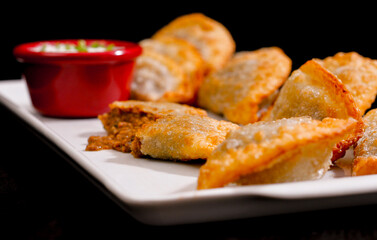Deliciosos pasteis de carne, camarão, queijo com creme de queijo gorgonzola em recipiente branco em fundo escuro.