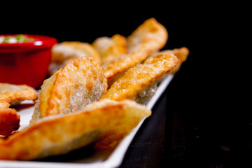 Deliciosos pasteis de carne, camarão, queijo com creme de queijo gorgonzola em recipiente branco em fundo escuro.