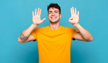 young man smiling and looking friendly, showing number nine or ninth with hand forward, counting...
