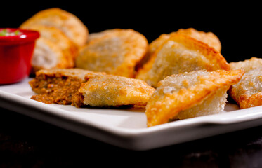 Deliciosos pasteis de carne, camarão, queijo com creme de queijo gorgonzola em recipiente branco em fundo escuro.