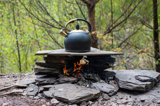 Close up shot of a round iron kettle filled with water, heating up on a campfire built on the shore of a river in the woodlands. - Powered by Adobe