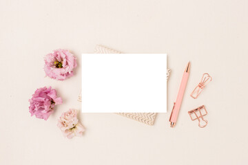 Blank paper card mockup, stationery and eustoma flowers on a beige background. Feminine workspace with copyspace. Cute springtime concept.