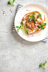 Tasty and healthy breakfast or lunch. Toast with tuna, ricotta cheese, and herbs in a white plate on a gray background top view. Mediterranean style breakfast. Free space for text.