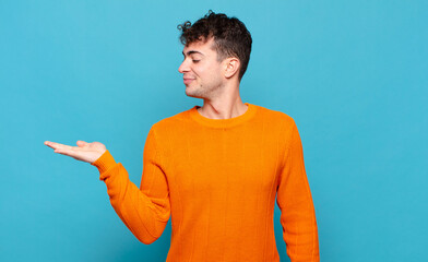 young man feeling happy and smiling casually, looking to an object or concept held on the hand on...