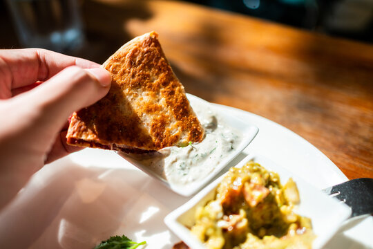 Hand holding Vegan Quesadilla: grilled whole-wheat tortilla filled with sweet potato and red bean, vegan quesso cheese, dipping with Tzaziki sauce. Creative Mexican vegan food.