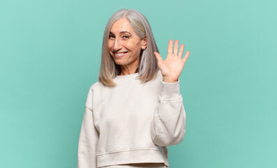 middle age woman smiling happily and cheerfully, waving hand, welcoming and greeting you, or saying goodbye © kues1