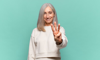 middle age woman smiling and looking friendly, showing number three or third with hand forward,...