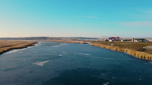 Beautiful winter landscape with frozen water in river and buildings far away under blue sky. Cold season