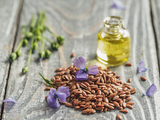 Flax seeds and flax oil. Brown linen seeds, flaxseed oil and blue flax flowers on old gray wooden background. Copy space