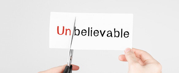 Scissors cutting white paper with the text unbelivable, change word to belivable.
