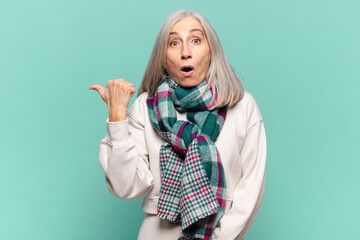 middle age woman looking astonished in disbelief, pointing at object on the side and saying wow,...