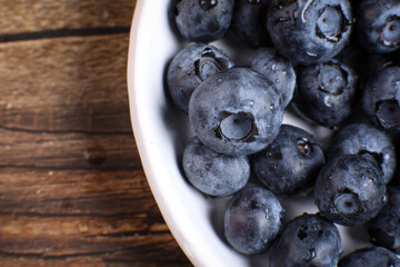 Top view of a white plate full of blueberries on a wooden table. Fruit vitamin.
