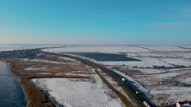 Winter highway with moving trucks near solar panels stanton and snow on hills. Drone shoots video of energy saving and concept of alternative power source