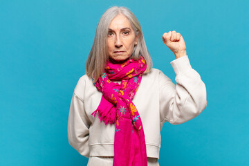 middle age woman feeling serious, strong and rebellious, raising fist up, protesting or fighting...