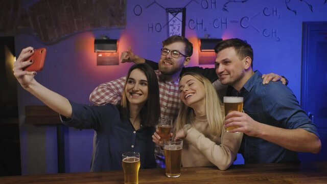 Friends in pub on bar counter with beer glasses in hands make group selfie. Social life