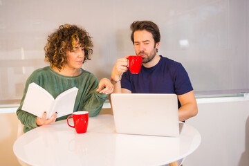 Lifestyle, a young Caucasian couple in pajamas having breakfast in the kitchen, a girl reading a book and a boy reading emails on the computer