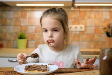 Little girl overeating chocolate cream by spoon