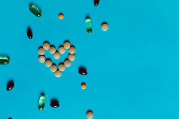 Heart of red pills decorated with different vitamins on a blue background. Chelated iron, Omega-3, zinc. Valentine's Day concept, top view, flat lay, place for text 