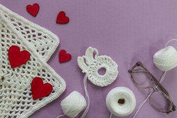 White yarn with knitting motifs, glasses and red hearts on a pastel background, a place for text-the concept of preparing gifts with your own hands for Valentine's Day