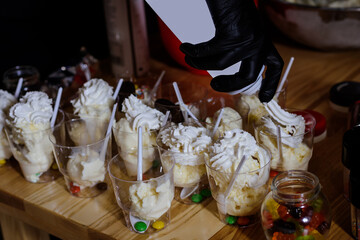 Ice cream into plastic glasses, chef's hands in black glove.