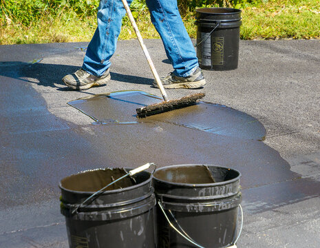 Do it yourself home maintenance. Driveway resealing repair. Homeowner smoothing out blacktop sealant on an asphalt driveway