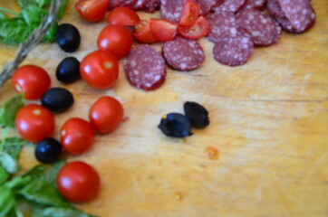 girl cuts vegetables, olives or tomatoes on a wooden board to make pizza Margherita pizza with utensils and vegetable on slate plate
