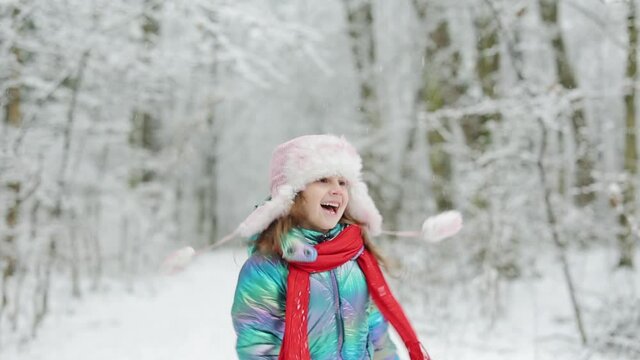 Little girl jumping on the snow wearing snow clothes. Funny little girl in a colorful knitted hat and warm coat playing with snow. Kids play outdoors in winter. Children having fun at Christmas time