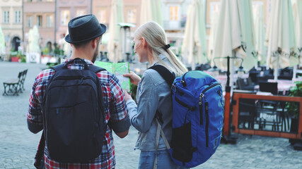 Back view of young man and woman with bags checking map on central city square. They discussing their new destination.