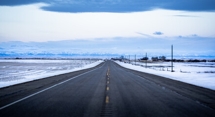 Fototapeta premium A snowy owl sits perched on top of a power pole along a hi way facing the distant West slopes of the Canadian Rocky Mountains.