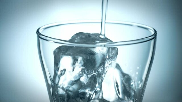 Pouring a water into a glass with ice cubes isolated. Slow motion.