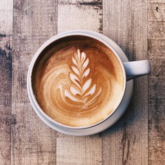 Cup of freshly made delicious cappuccino coffee with latte art on wooden background, top view. Copy...