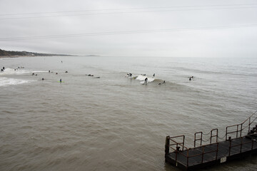 Bournemouth surfers in winter in sea with clouds overhead 