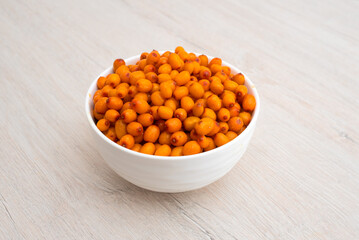 Bowl with sea buckthorn berries on wooden background. Side view. 