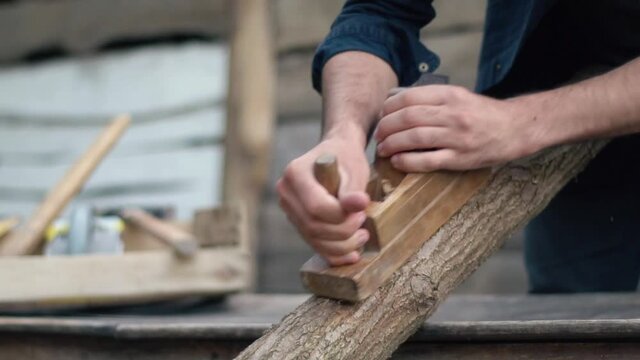 The hands of a carpenter who cut a log with a plane. The hard work of a handyman in the village