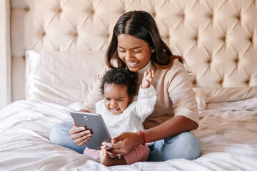 Mixed race Indian black mother with toddler baby girl watching cartoons on tablet. Ethnic...