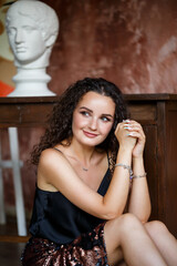 Portrait of a young charming woman with curly hair, fair-skinned girl in a black top and with a smile on her face