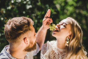 Happy couple spend time together and feed each other grapes in summer outdoors